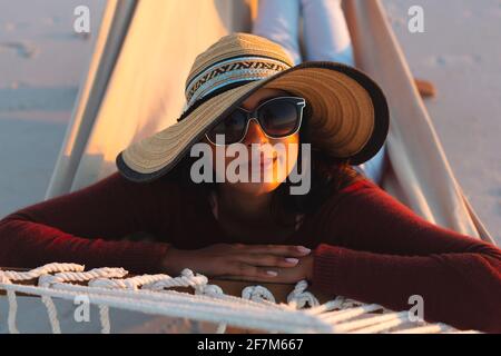 Portrait of happy mixed race woman on beach holiday looking to camera lying in hammock during sunset Stock Photo