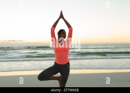 Mixed race woman on beach practicing yoga at sunset Stock Photo