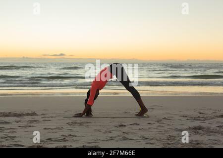 Mixed race woman on beach practicing yoga during sunset Stock Photo