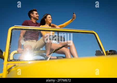 Happy caucasian couple sitting in beach buggy by the sea taking selfie Stock Photo