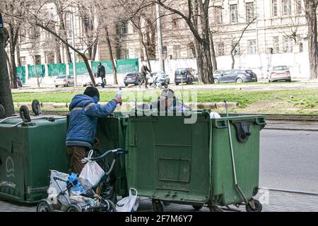 Dnepropetrovsk, Ukraine - 04.06.2021: Dirty tramps search for food and used PET bottles in a trash bin on the street. Homeless men have no money or ho Stock Photo