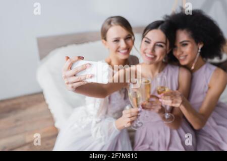joyful woman taking selfie with bride and african american friend on blurred background Stock Photo