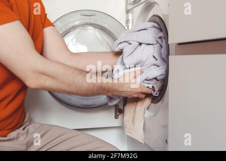 Man loading color clothes and towels into built-in washing machine Stock Photo