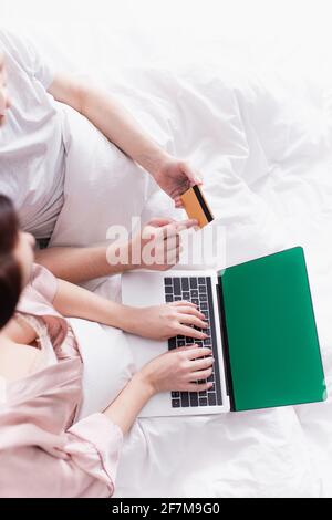 Top view of couple using laptop with green screen and credit card on bed Stock Photo
