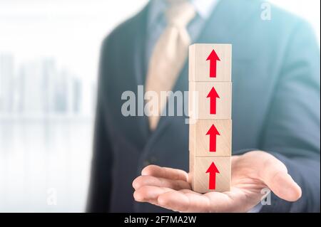 Profit Chart Made Of Wooden Blocks. Businessman hold wooden cubes with red arrow sign on blurred office background. Business development to success an Stock Photo