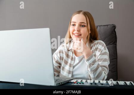 Woman learns to play piano online using laptop. Woman plays keyboard instrument on synthesizer piano during online lesson with teacher. Online concert Stock Photo