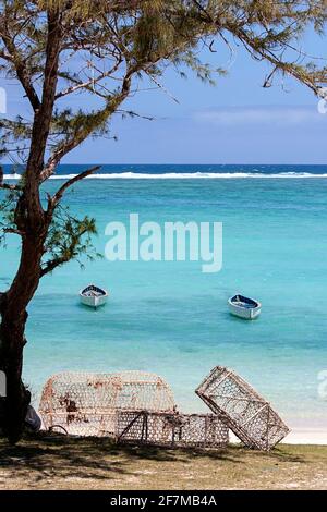 Fishing traps under a tree on a beach, fishing boats in the colourful Indian Ocean, coral reef in the background, Rodrigues Island, Mauritius Stock Photo