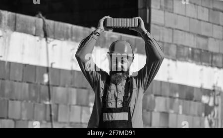 Lightweight brick made from expanded clay aggregate. Element in masonry construction. Builder hold brick. Bearded man wear hard hat at construction Stock Photo