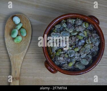 Habas a la Catalana, stew of beans in a clay bowl decorated with raw beans on a wooden spoon. Top view Stock Photo