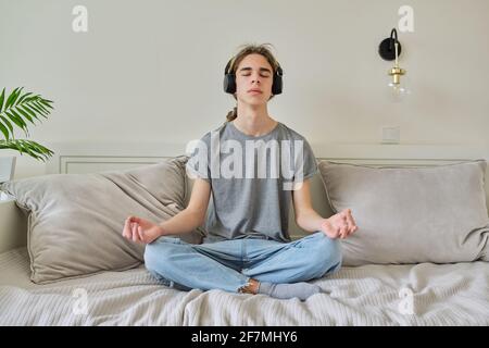 Male teenager sitting in lotus position on bed relaxing meditating Stock Photo