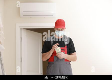Builder in overalls and protective mask, transferring his salary for work performed on the construction site. Close-up view focused on money. Stock Photo