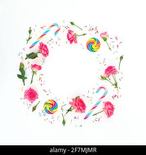 Round frame made of roses flowers with bright sugar candies on white background. Flat lay, top view. Stock Photo