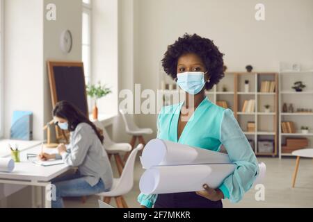 Portrait of african american woman in protective mask with blueprints in office Stock Photo