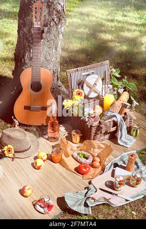 Vintage picnic basket, hamper with baguette and lemonade outdoors on a grass with cheese, mozzarella, tomatoes, cherries, vine. Guitar, snacks on Stock Photo