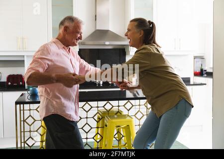 Happy caucasian senior couple in kitchen having fun dancing and smiling Stock Photo