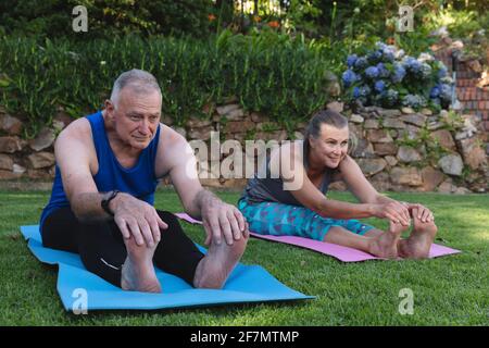 Happy caucasian senior couple exercising in garden, sitting on mats practicing yoga Stock Photo