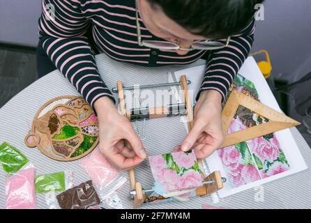 Weaving from beads. Close-up - a woman's hands are stringing beads on a thread, making jewelry. The woman is fond of weaving from beads. Stock Photo