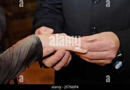Groom places gold ring on bride's hand on their wedding day. Stock Photo