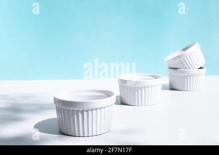 Stack of four white ceramic bowls on blue pastel background with hard shadows. Creative kitchen tableware Stock Photo