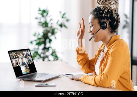 African American female student listens to an online lesson using a laptop and a headset, watches a webinar, studies remotely, the teacher and other students are on the laptop screen. E-learning Stock Photo