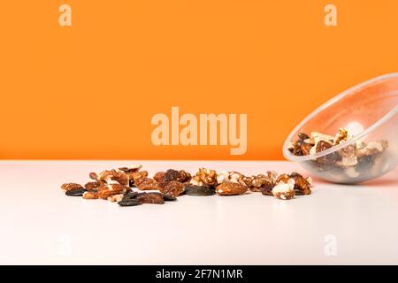 Various nuts spilled from a cup on the white table against bright orange background. Selective focus, minimalistic, vivid colors. Stock Photo