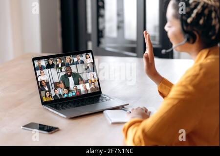 Online business group brainstorm by video conference. Side view of african american young woman, communicates with business partners by video call uses laptop, multiracial colleagues on laptop screen Stock Photo