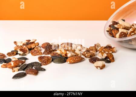 Various nuts spilled from a cup on the white table against bright orange background. Selective focus, minimalistic, vivid colors. Stock Photo