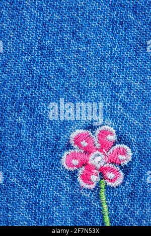Embroidered pink flower on fragment of  blue denim jeans texture Stock Photo