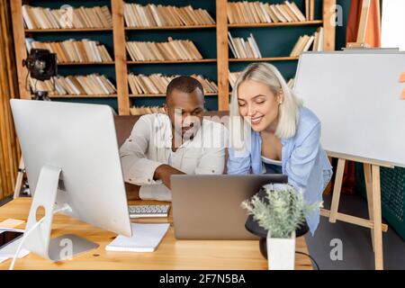 Happy business partners working together on project in office, smiling, using laptop. Multiracial successful colleagues discussing new startup Stock Photo