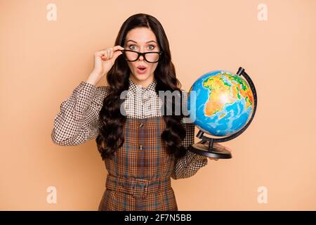 Portrait of lovely amazed wavy-haired teacher holding in hands globe explore world pout lips isolated on beige pastel color background Stock Photo