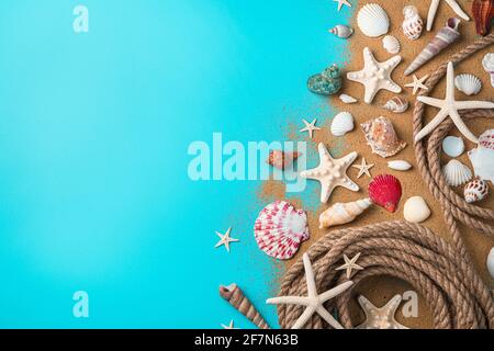 Seashells of various kinds, starfish and a rope on the sand on a blue background. Top view, copy space. Stock Photo