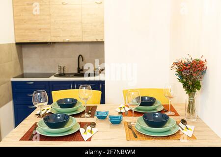 Wooden dining table in a modern dining room with a vase of plants, and a table set, ready to be served with food. Stock Photo