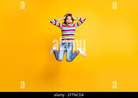 Full length body size photo of jumping high crazy schoolgirl keeping head with hands shouting isolated on vibrant yellow color background Stock Photo
