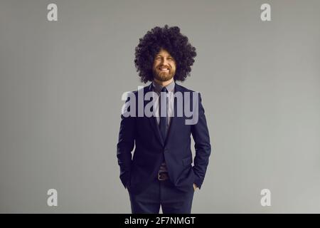 Happy guy in elegant suit and crazy curly wig standing hands in pockets and smiling Stock Photo