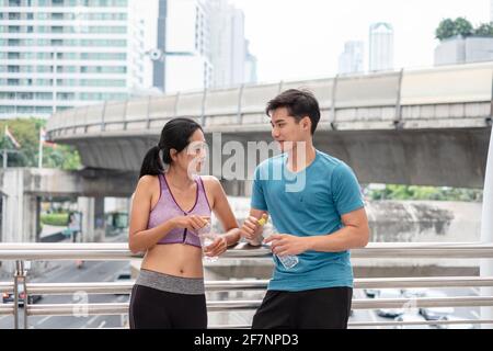 Young asian couple athletes standing resting with water bottle after exercise on the bridge in urban Stock Photo