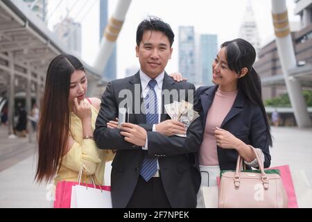 Asian businessman confident and flirting holding credit card and dollar cash standing between beautiful young asian women in urban Stock Photo