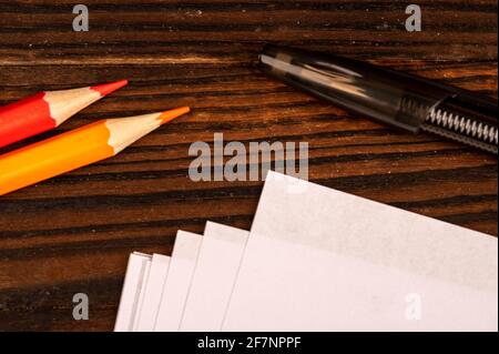 Colorful pencils, ballpoint pens, and white sheets of paper on a wooden table. Close-up selective focus. Stock Photo
