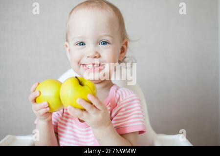 A little girl tastes, examines and plays with fresh apples with pleasure and interest. Stock Photo
