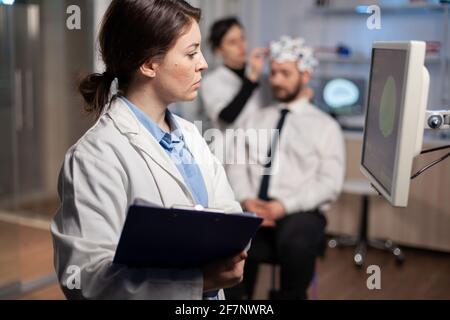 Neurologist scientist looking at brain tomography of patient with headset, high tech scan on monitor screen. Doctor adjunsting electrodes. Modern neuroscience. Stock Photo