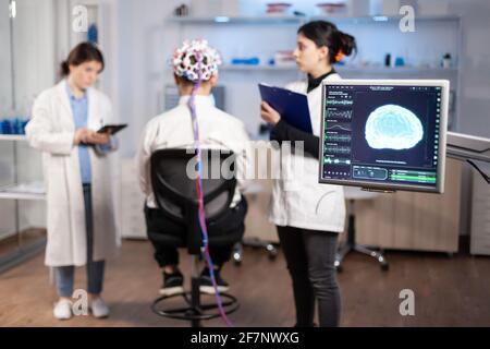 Man patient wearing performant eeg headset scanning brain electrical activity in neurological research laboratory while medical researcher controlling it, examining nervous system, nurse taking notes Stock Photo