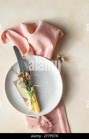 Romantic or spring table setting. Knife and fork, little pink flowers and linen napkin on a plate, light concrete background. Flat lay. Selective focu Stock Photo
