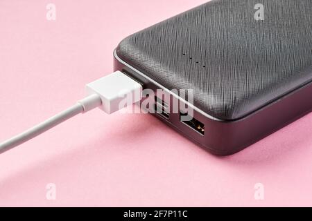 USB connector is connected to Power bank on a pink background. Charging gadgets. Close-up, selective focus Stock Photo