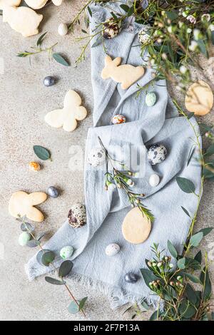Easter cookies with candies shaped eggs, floral decor and quail eggs on linen napkin, stone background. Holiday concept. Selective focus. Top view. Stock Photo