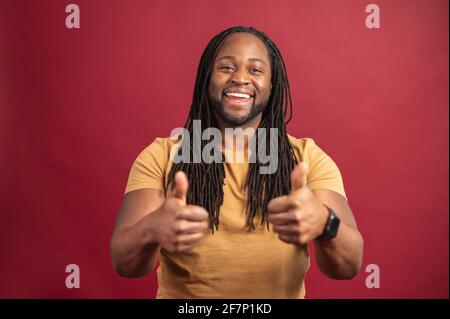Black man stands and shows sign that everything under control, portrait of charismatic african american bearded man, say ok smiling assured confident you look perfect, standing pleased red background Stock Photo