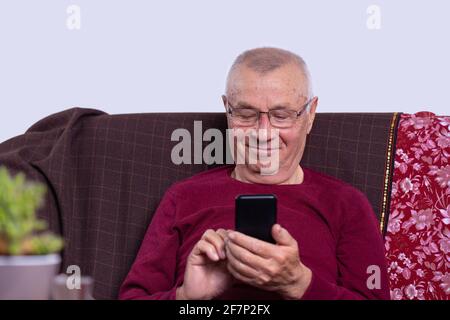 Smiling older man holding phone, using mobile device apps, looking at screen, happy mature male chatting online, texting, writing message, having fun Stock Photo