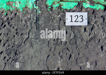 Asphalt background with a turquoise green strip on top and a white screwed-in tile with number 123 printed on it Stock Photo