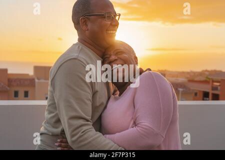 Happy Latin senior couple having romantic moment embracing on rooftop during sunset time - Elderly people love concept Stock Photo