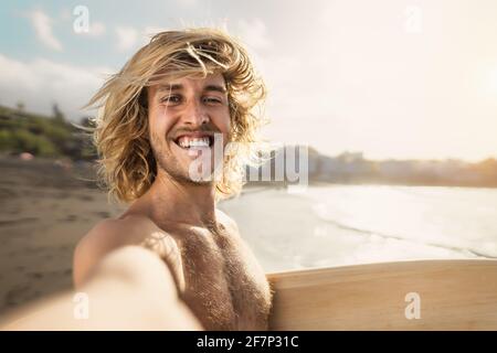 Young surfer man taking selfie while having fun surfing on sunny day - Youth people lifestyle and extreme sport concept