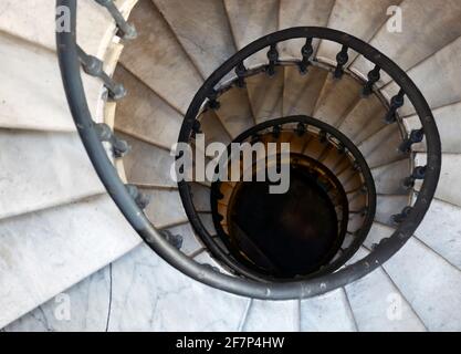 Old spiral staircase with marble steps and wrought iron handrail. Architecture and curved shapes. Top down view. Height and vertigo effect