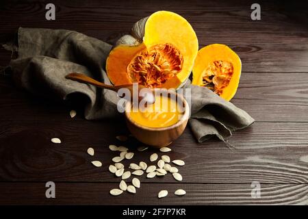 Bowl of pumpkin cream soup with fresh cut pumpkins on dark wooden background Stock Photo